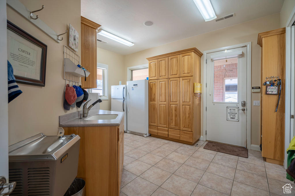 Kitchen featuring light tile floors, sink, white refrigerator, and a healthy amount of sunlight