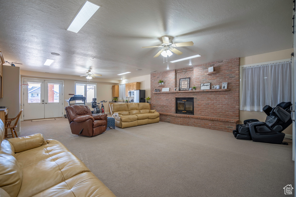 Carpeted living room featuring a textured ceiling, a skylight, french doors, a brick fireplace, and ceiling fan