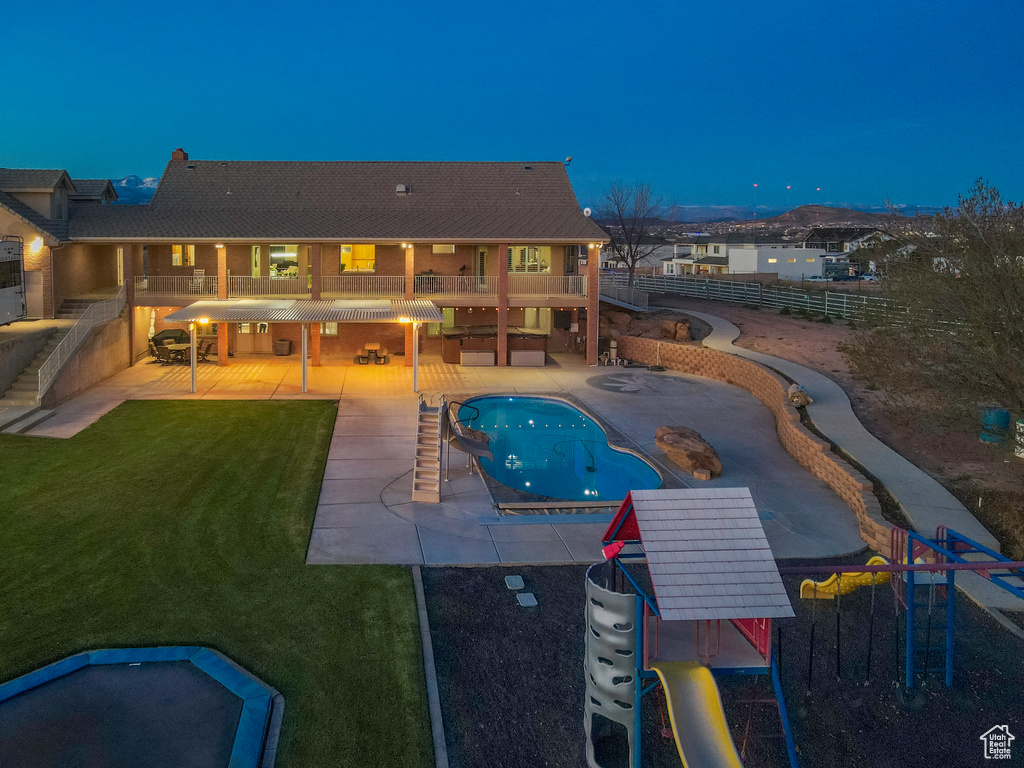 Pool at night with a patio area, a jacuzzi, a playground, and a yard