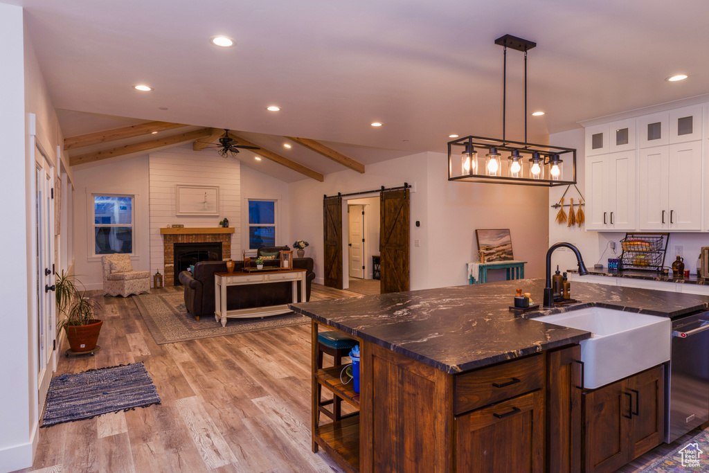Kitchen with a barn door, white cabinets, hanging light fixtures, light wood-type flooring, and an island with sink