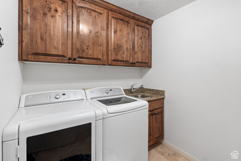 Laundry room with light tile flooring, cabinets, a textured ceiling, sink, and independent washer and dryer