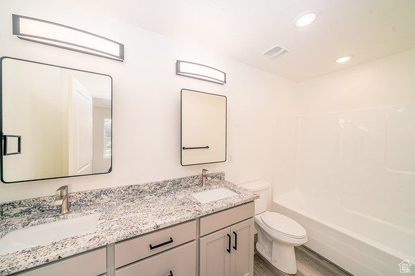 Full bathroom featuring double vanity, wood-type flooring, shower / bathtub combination, and toilet