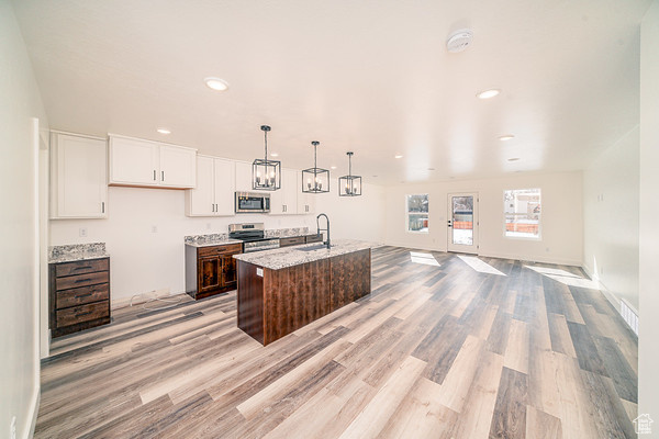 Kitchen featuring appliances with stainless steel finishes, white cabinets, light hardwood / wood-style floors, pendant lighting, and an island with sink