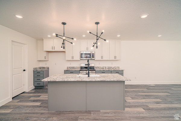 Kitchen featuring a notable chandelier, an island with sink, dark hardwood / wood-style floors, decorative light fixtures, and white cabinets