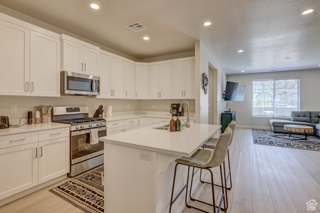 Kitchen with sink, white cabinets, appliances with stainless steel finishes, light wood-type flooring, and a breakfast bar area