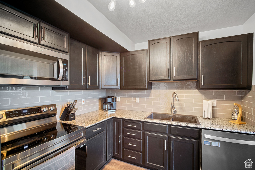 Kitchen with appliances with stainless steel finishes, dark brown cabinets, sink, and backsplash