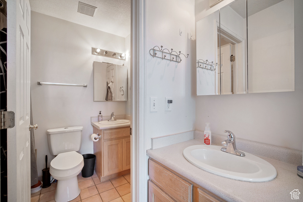 Bathroom featuring double vanity, toilet, a textured ceiling, and tile floors