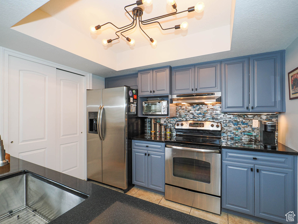 Kitchen with stainless steel appliances, a tray ceiling, light tile floors, and backsplash
