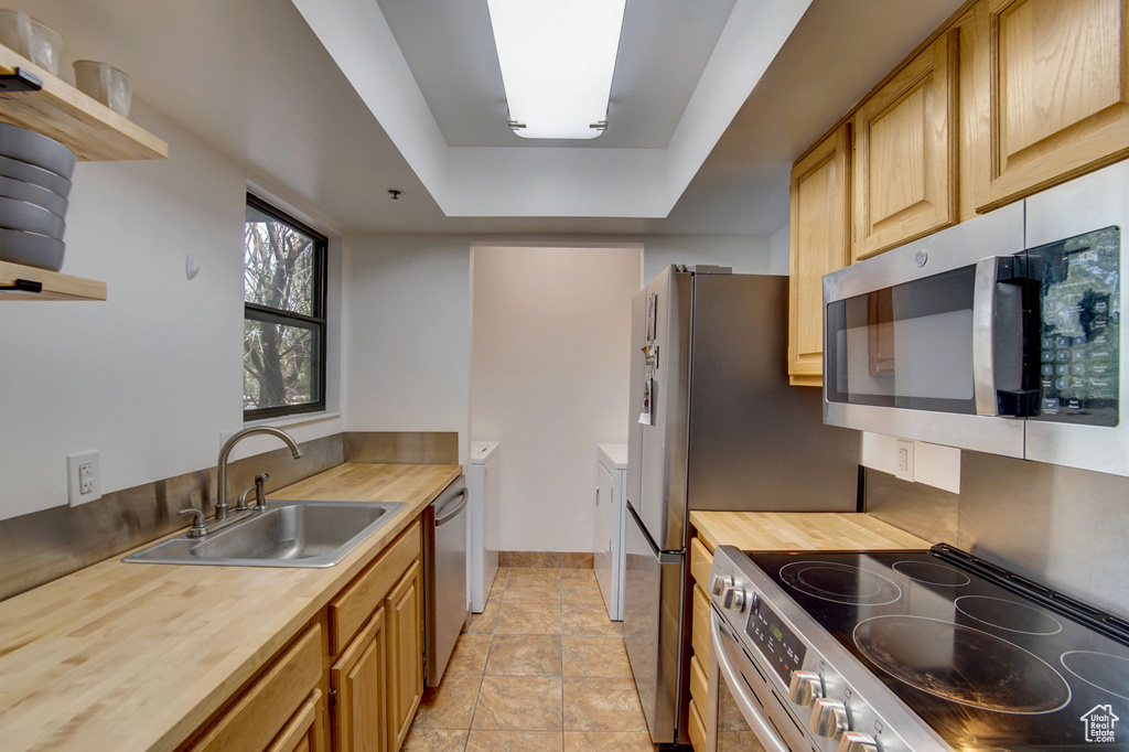 Kitchen featuring sink, wooden counters, a tray ceiling, light tile floors, and stainless steel appliances