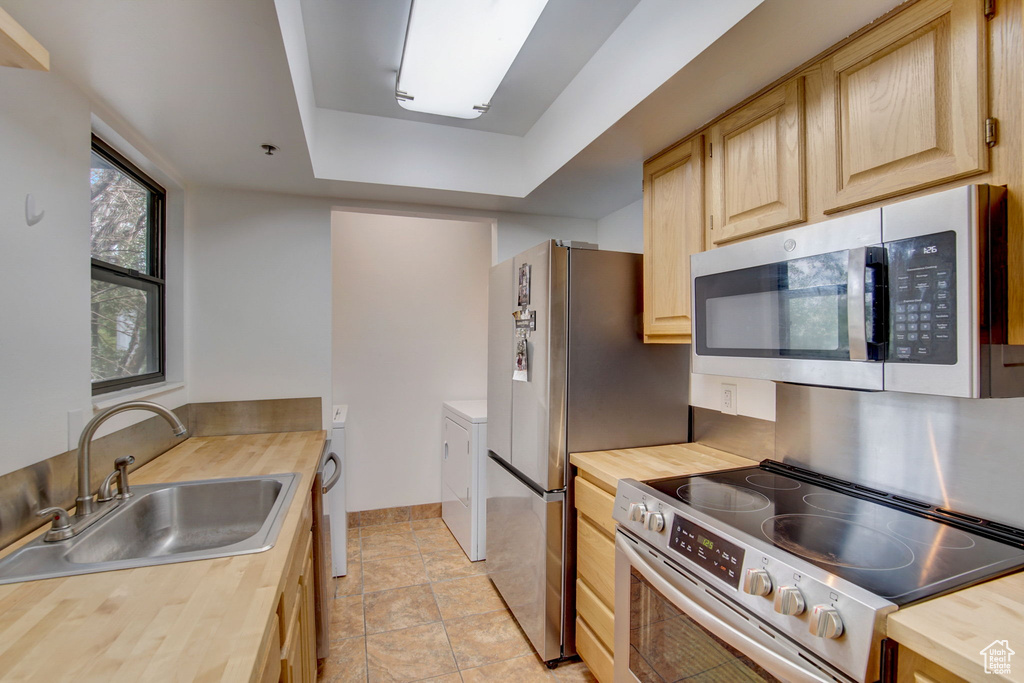 Kitchen with a tray ceiling, light tile flooring, separate washer and dryer, sink, and appliances with stainless steel finishes