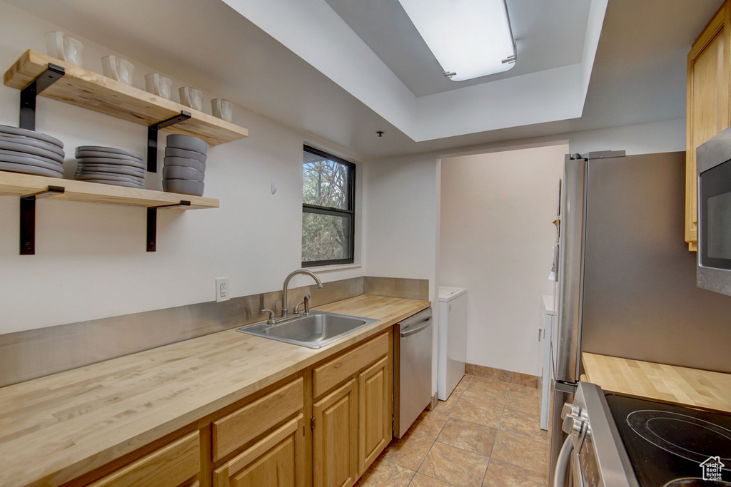 Kitchen featuring stainless steel dishwasher, light tile flooring, stove, sink, and butcher block countertops