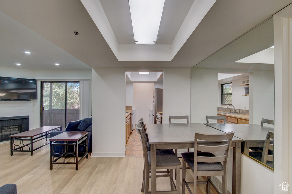 Dining space featuring a tray ceiling, sink, a brick fireplace, and light hardwood / wood-style flooring