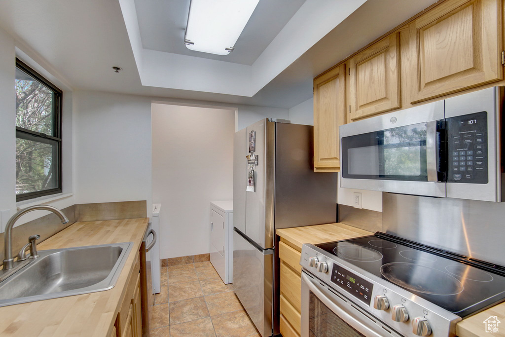 Kitchen with a raised ceiling, light tile floors, stainless steel appliances, sink, and light brown cabinets