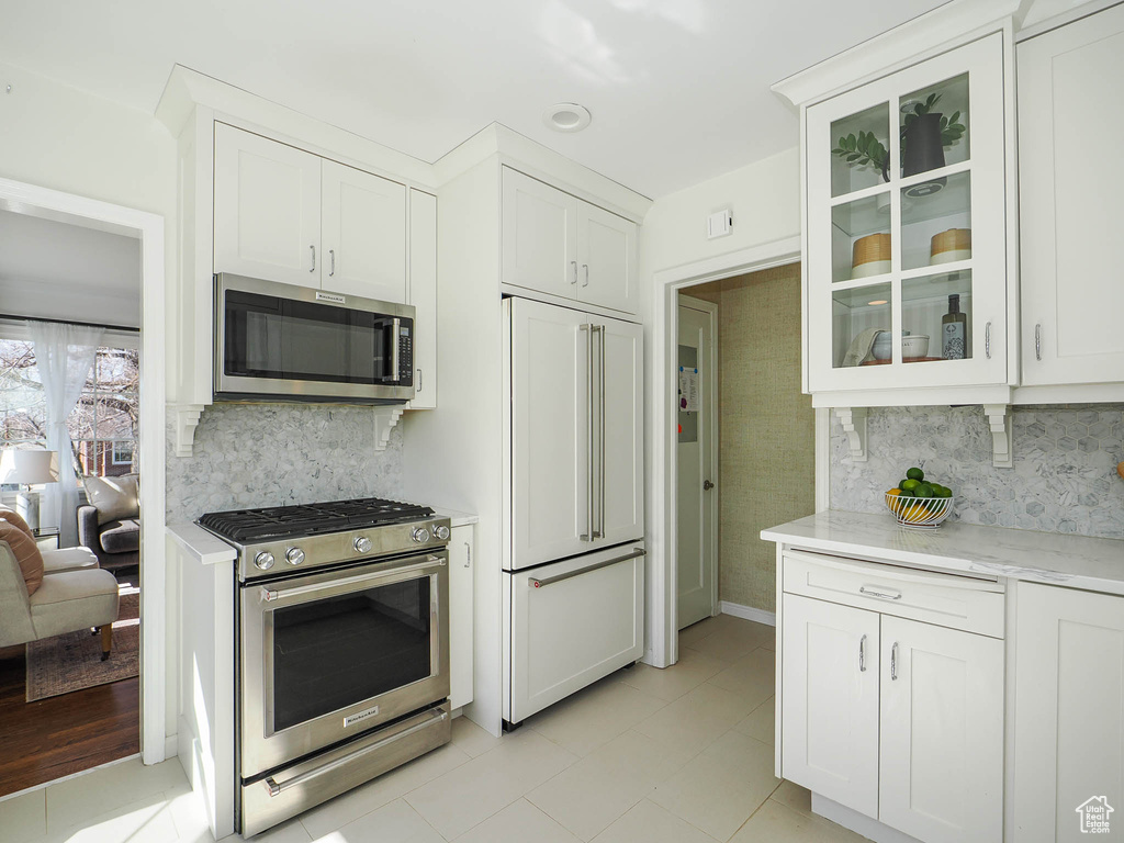 Kitchen featuring white cabinets, light tile floors, backsplash, stainless steel appliances, and light stone counters