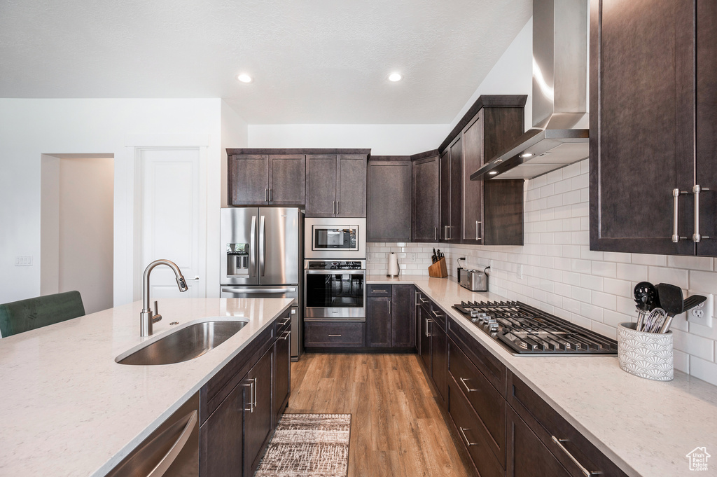 Kitchen with sink, wall chimney exhaust hood, appliances with stainless steel finishes, light wood-type flooring, and backsplash