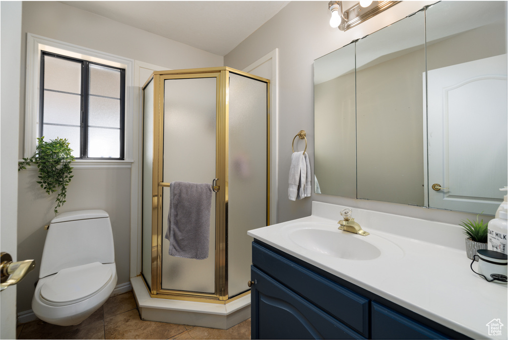 Bathroom with toilet, tile flooring, large vanity, and a shower with door