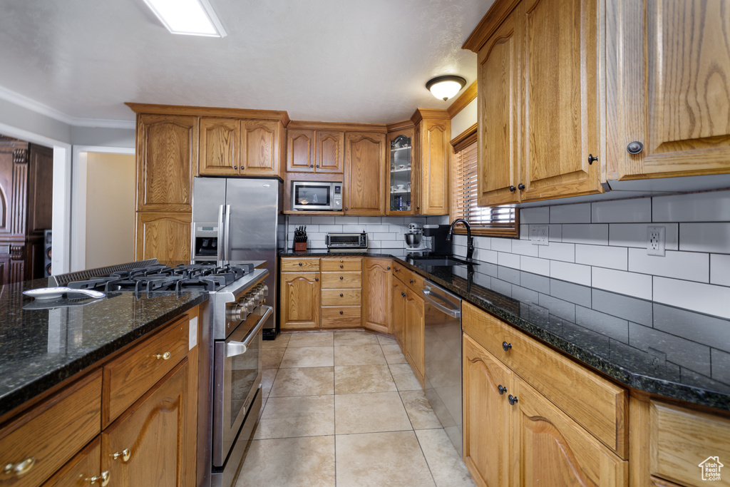Kitchen featuring sink, tasteful backsplash, dark stone counters, light tile floors, and stainless steel appliances