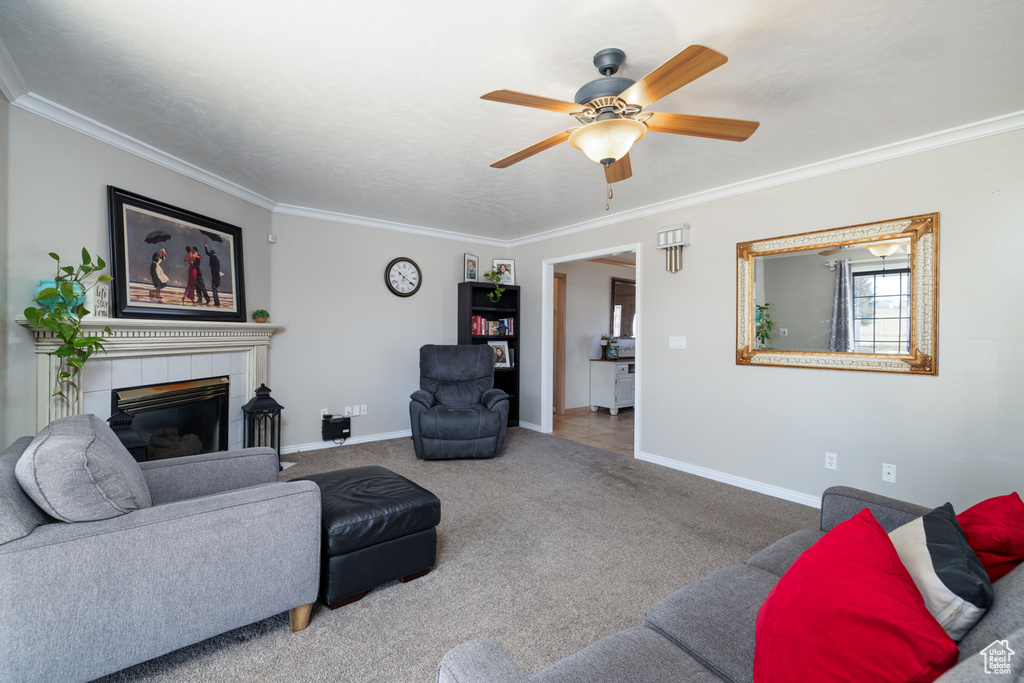 Carpeted living room with ornamental molding, a tiled fireplace, and ceiling fan