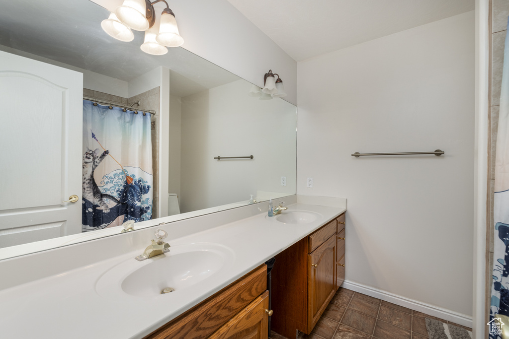 Bathroom with vanity with extensive cabinet space, dual sinks, toilet, tile flooring, and an inviting chandelier