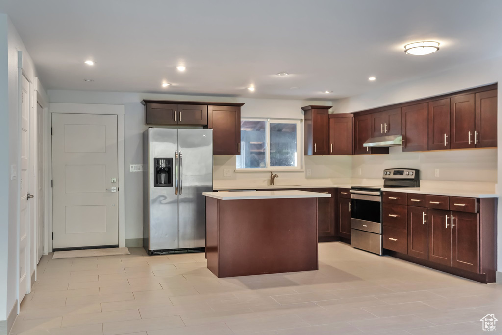 Kitchen featuring light tile flooring, sink, appliances with stainless steel finishes, a center island, and dark brown cabinets