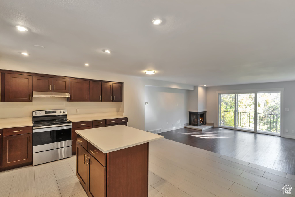 Kitchen with a kitchen island, dark brown cabinets, stainless steel electric range, and light tile flooring