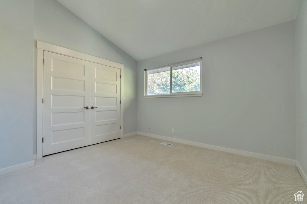 Unfurnished bedroom with vaulted ceiling, light colored carpet, and a closet