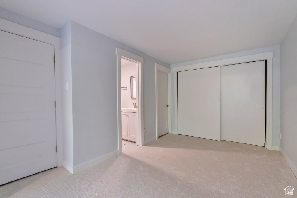 Unfurnished bedroom featuring ensuite bathroom, light colored carpet, a closet, and sink
