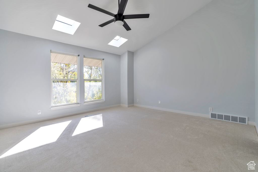 Spare room featuring light colored carpet, ceiling fan, and vaulted ceiling with skylight