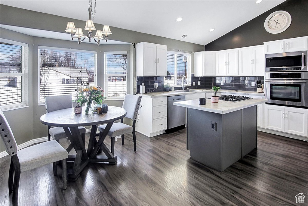 Kitchen featuring appliances with stainless steel finishes, hanging light fixtures, a notable chandelier, backsplash, and dark wood-type flooring