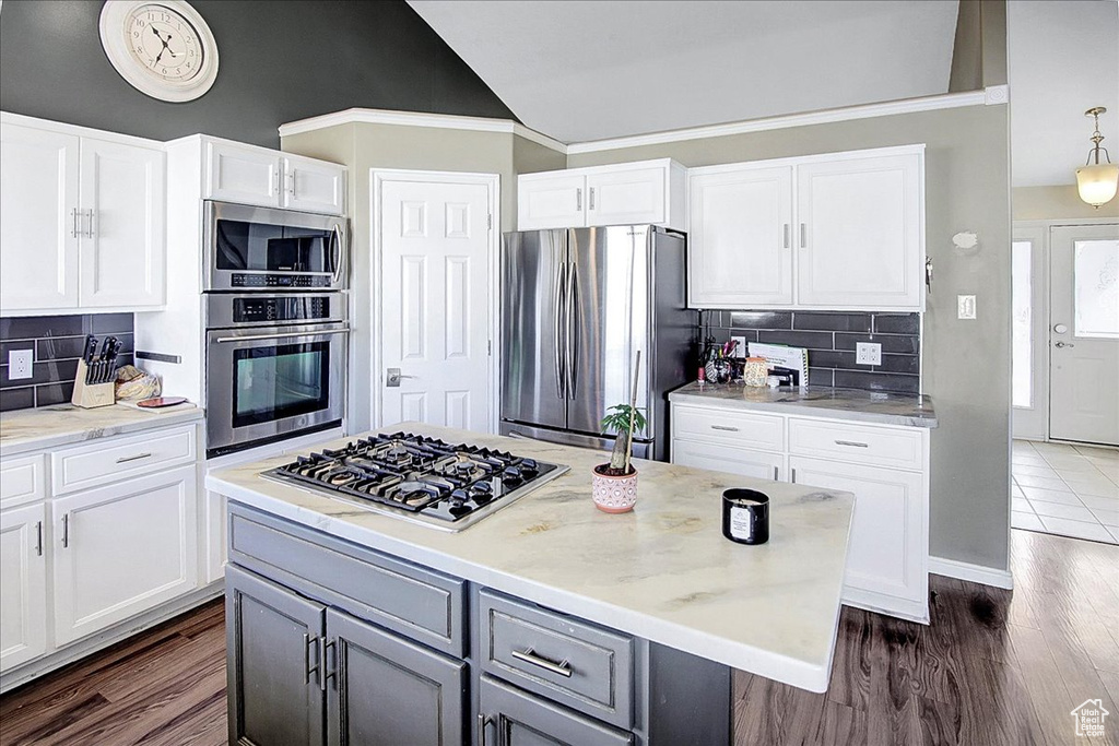 Kitchen with dark hardwood / wood-style flooring, ornamental molding, white cabinets, tasteful backsplash, and appliances with stainless steel finishes