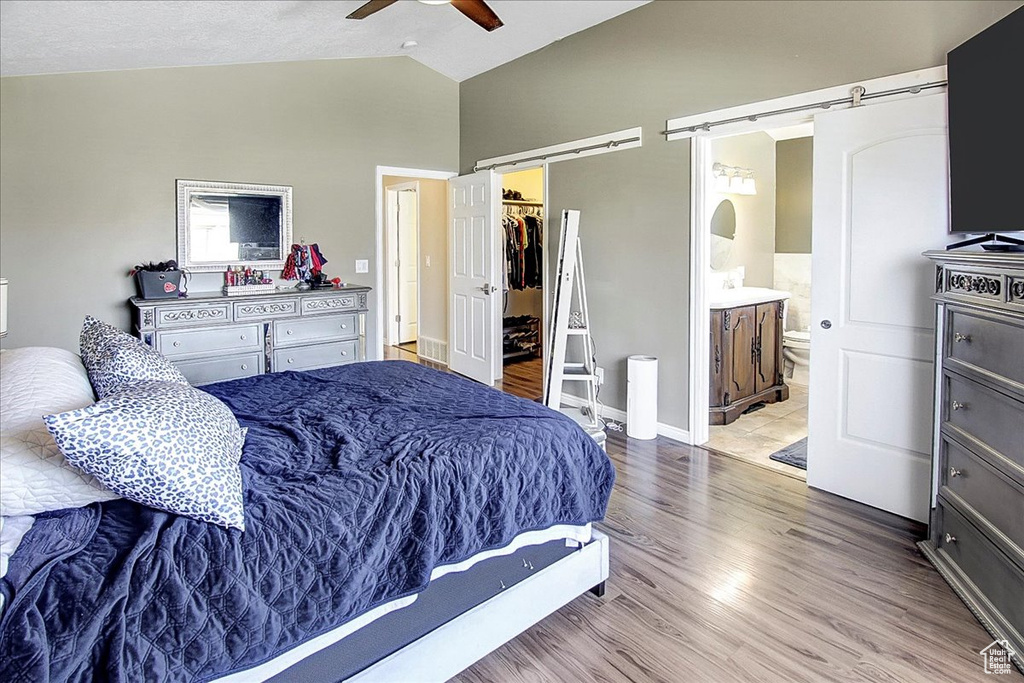 Bedroom with ensuite bathroom, ceiling fan, light hardwood / wood-style floors, and a barn door