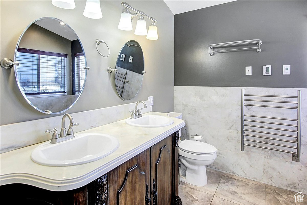 Bathroom featuring double sink vanity, tile walls, toilet, radiator, and tile floors