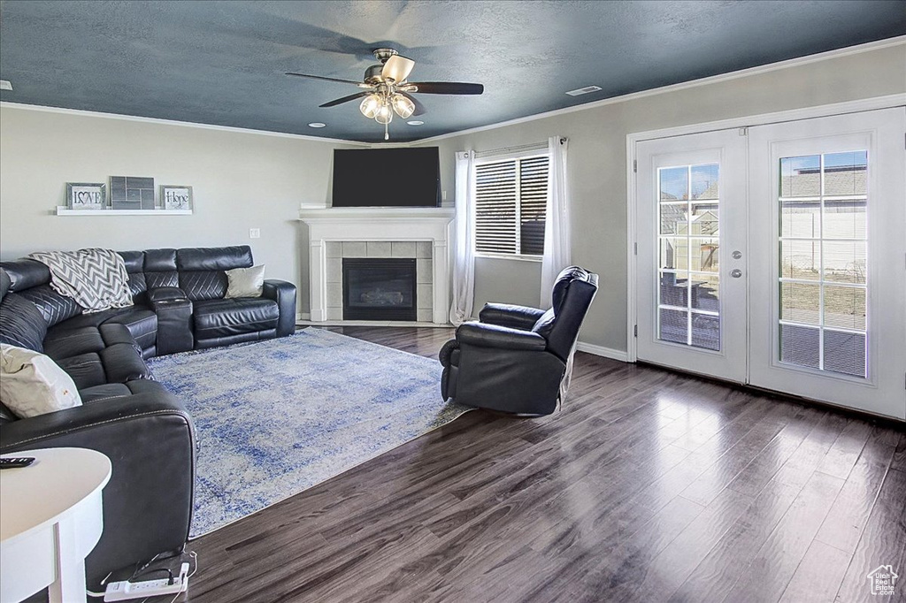 Living room featuring crown molding, ceiling fan, dark wood-type flooring, and a tile fireplace