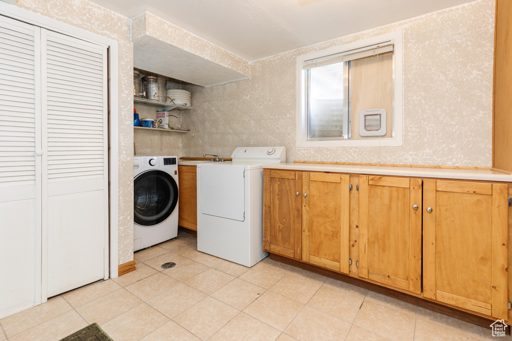 Laundry room with independent washer and dryer, light tile floors, and cabinets