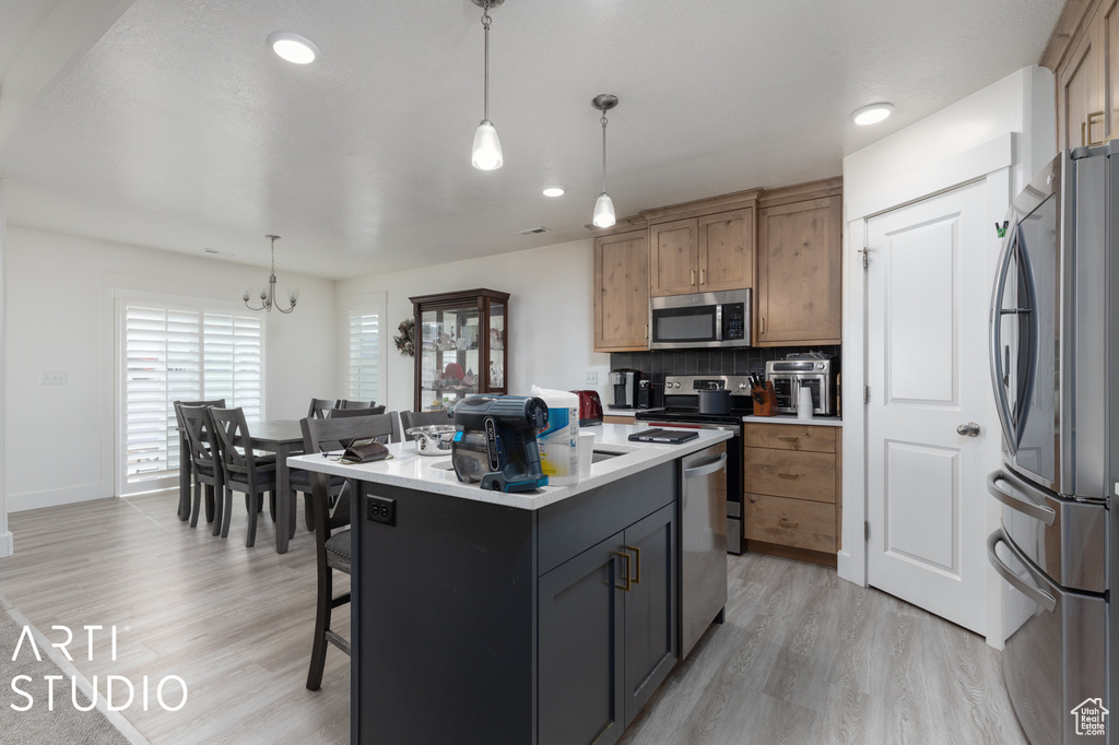 Kitchen with appliances with stainless steel finishes, light hardwood / wood-style flooring, a chandelier, and a kitchen island