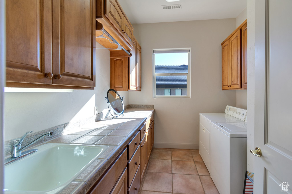 Laundry area with light tile floors, washer and dryer, sink, and cabinets