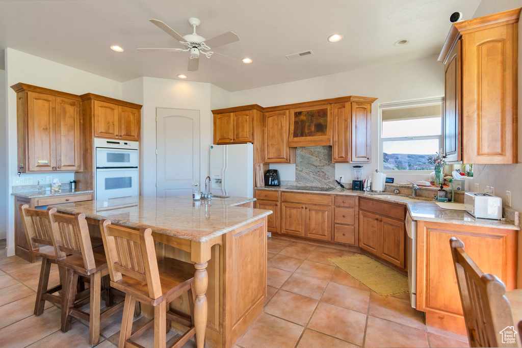 Kitchen with a kitchen breakfast bar, white appliances, tasteful backsplash, a center island with sink, and ceiling fan