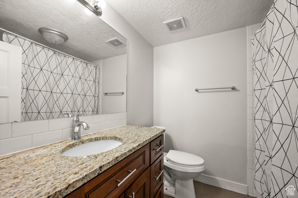 Bathroom with a textured ceiling, tile walls, tasteful backsplash, toilet, and oversized vanity