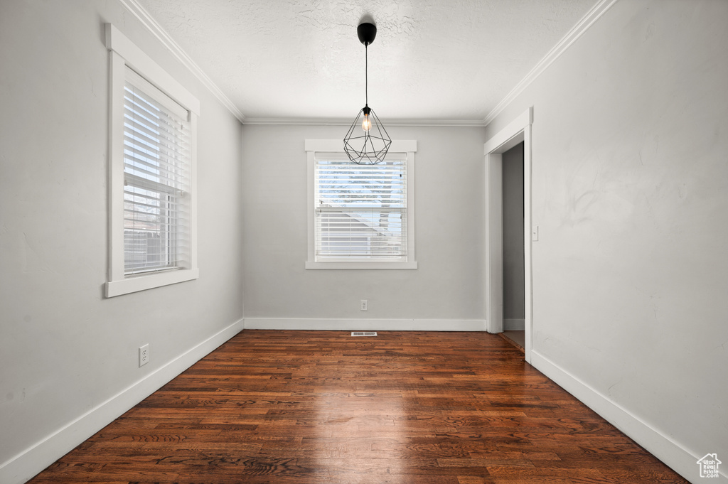 Empty room with dark wood-type flooring, a wealth of natural light, and ornamental molding
