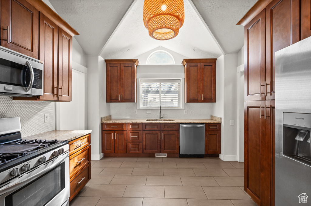Kitchen featuring appliances with stainless steel finishes, light tile floors, vaulted ceiling, and sink