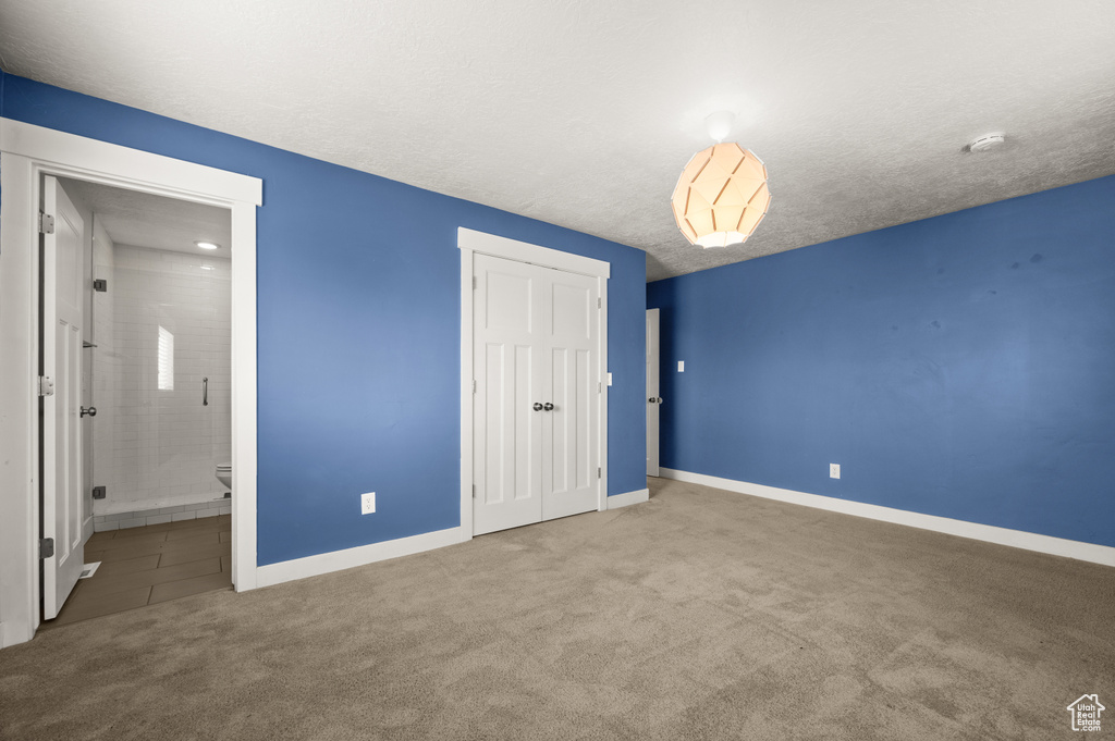 Unfurnished bedroom with light colored carpet, a textured ceiling, ensuite bath, and a closet