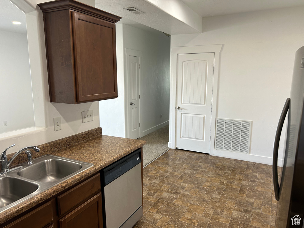 Kitchen featuring black refrigerator, dishwasher, sink, dark brown cabinets, and dark tile flooring