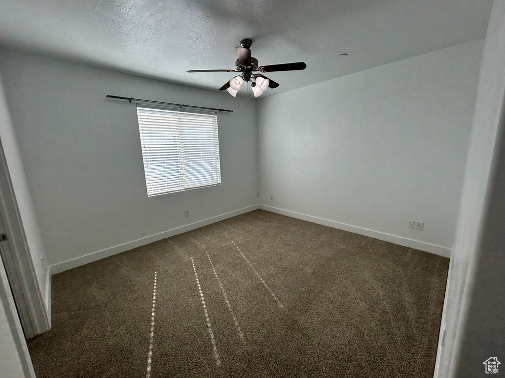 Unfurnished room with dark colored carpet, a textured ceiling, and ceiling fan