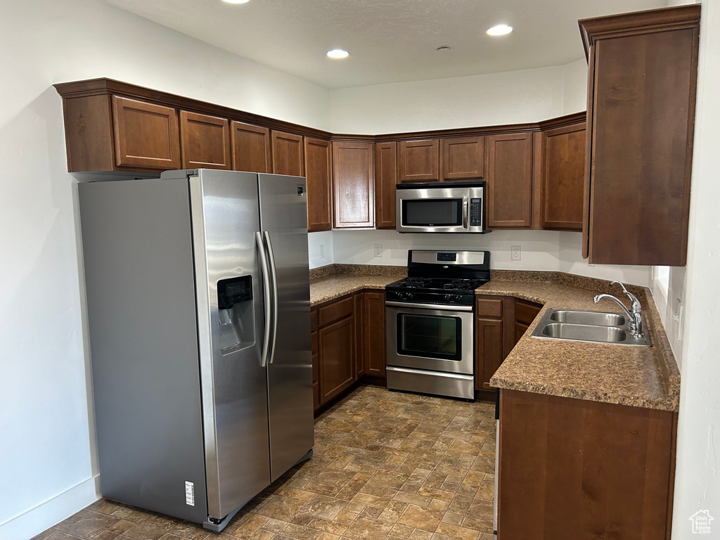 Kitchen featuring dark tile floors, sink, dark stone counters, stainless steel appliances, and dark brown cabinets