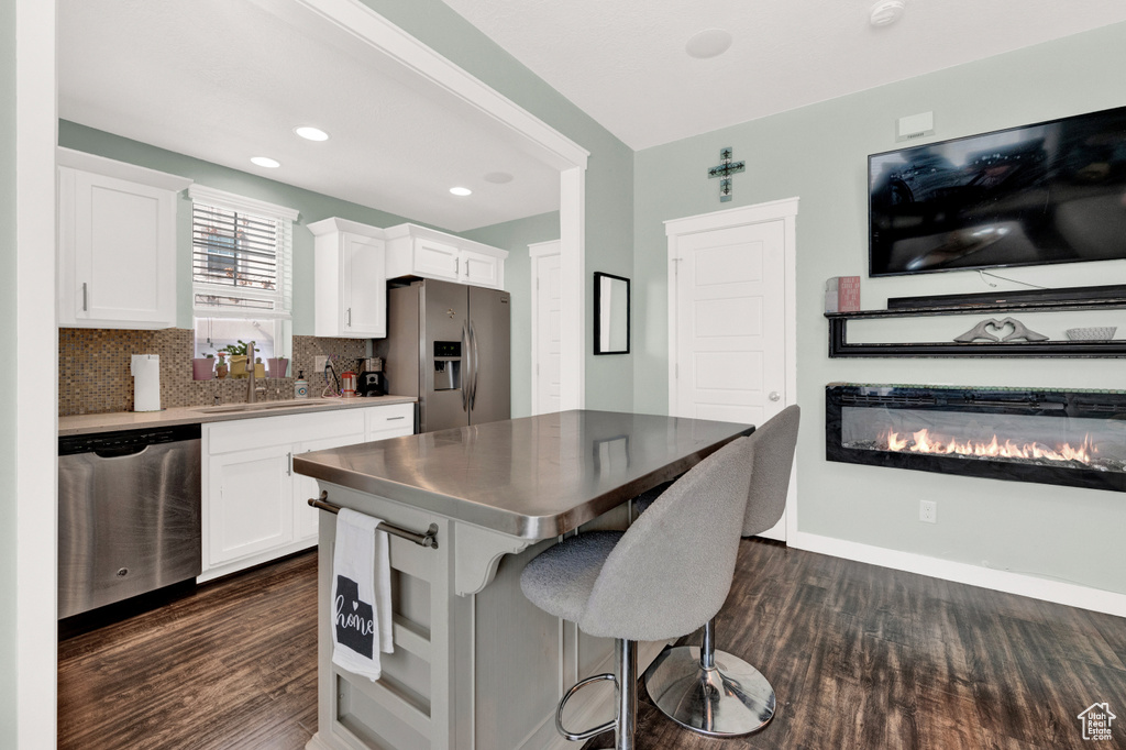 Kitchen with sink, dark wood-type flooring, a breakfast bar, white cabinetry, and stainless steel appliances