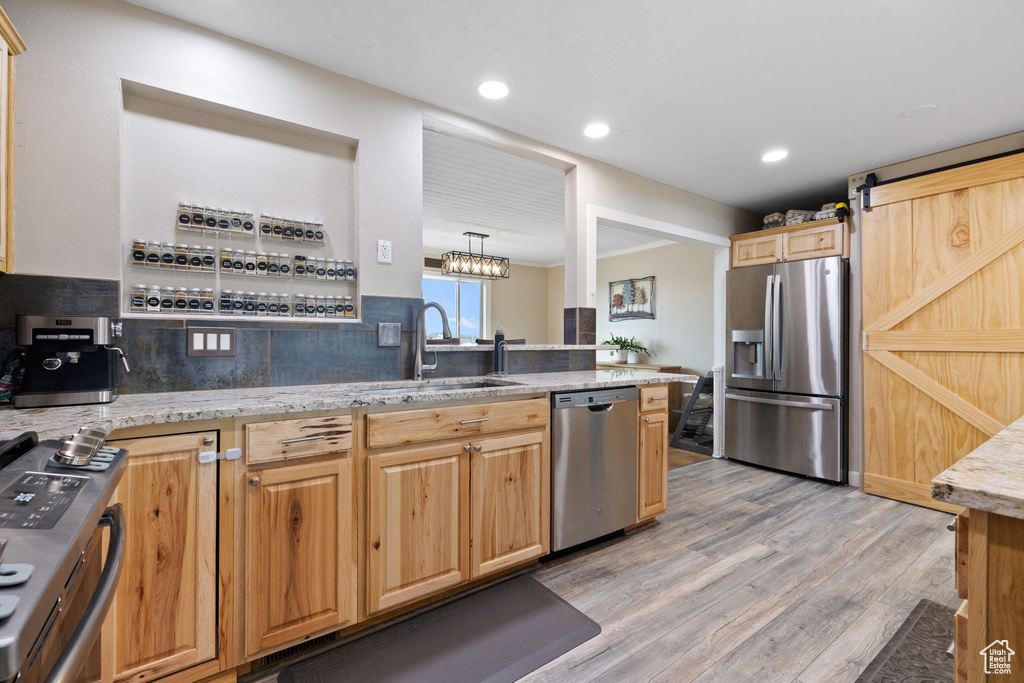 Kitchen featuring tasteful backsplash, sink, light wood-type flooring, hanging light fixtures, and stainless steel appliances