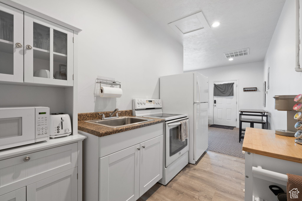 Kitchen with white cabinetry, white appliances, sink, and light wood-type flooring