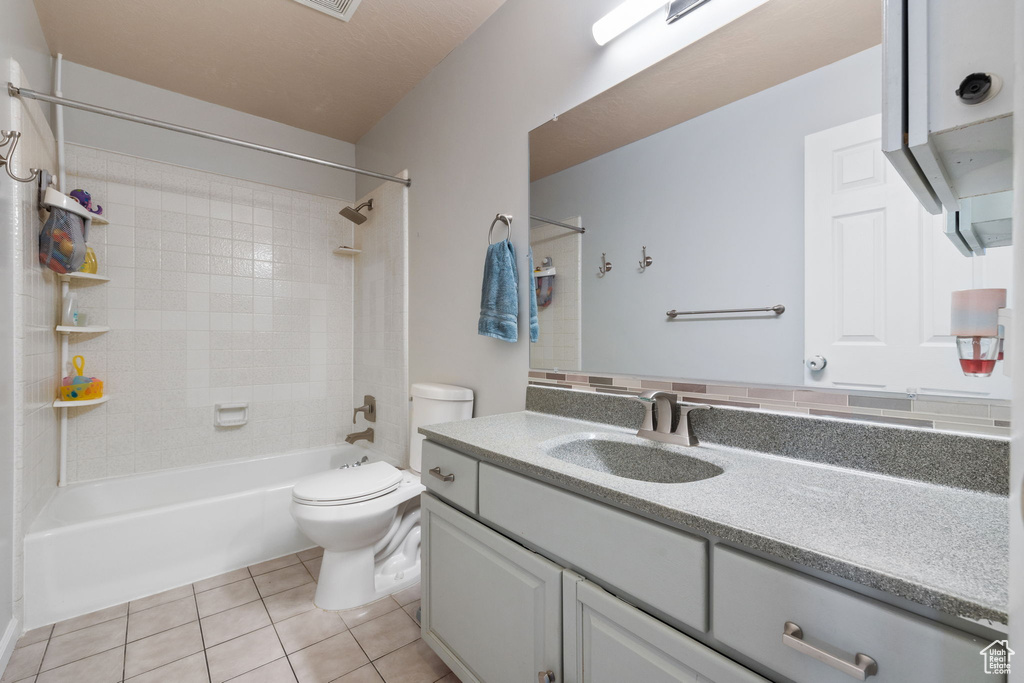 Full bathroom with tile floors, toilet, vanity with extensive cabinet space, and tiled shower / bath combo