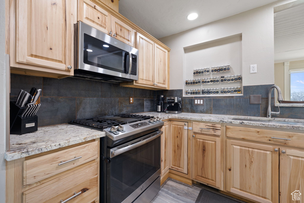 Kitchen featuring backsplash, stainless steel appliances, sink, and light stone counters