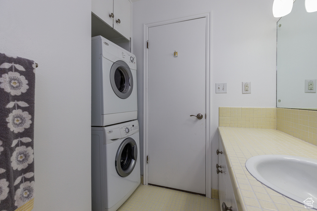 Washroom featuring stacked washer and dryer, light tile floors, and sink
